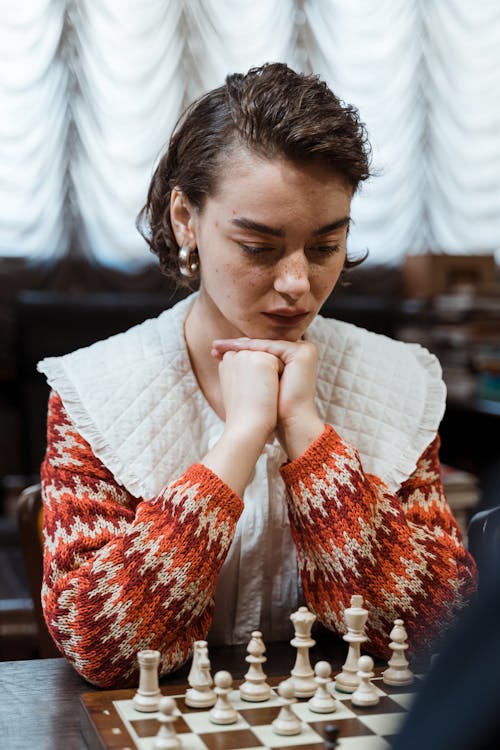 A Woman in Knitted Sweater Looking at the Chessboard