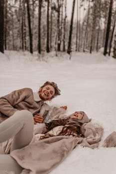 Happy couple laughing and playing in the snow, surrounded by a winter forest setting.