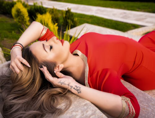 Alluring Woman in Red Dress Lying on Concrete Surface