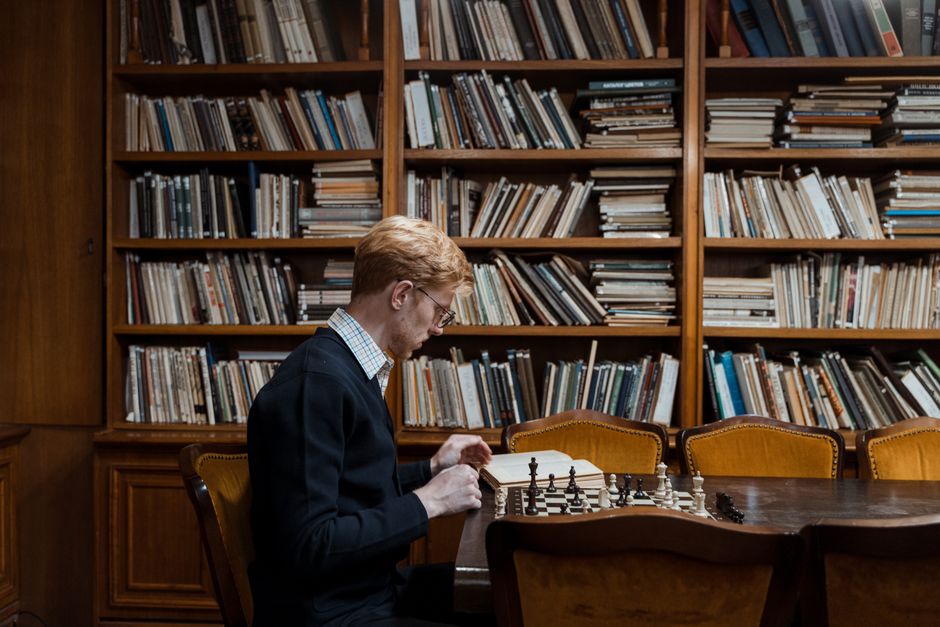 A man deeply focused on a chess game in a cozy library with wooden shelves.
