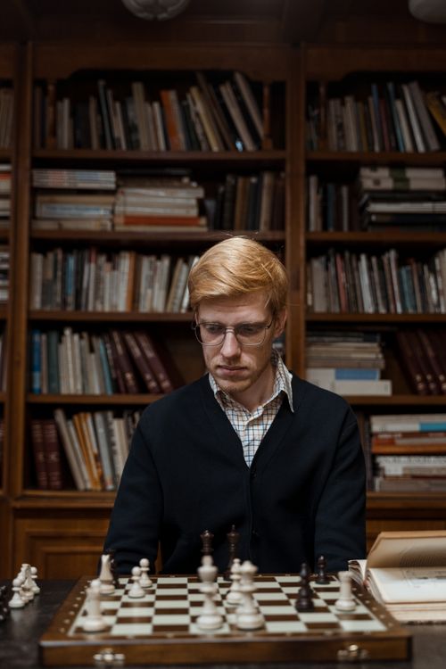 Free Focused man playing chess in a library setting, contemplating next move. Stock Photo