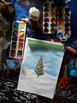 Overhead view of a creative workspace featuring paints, scissors, and a crafted holiday card.