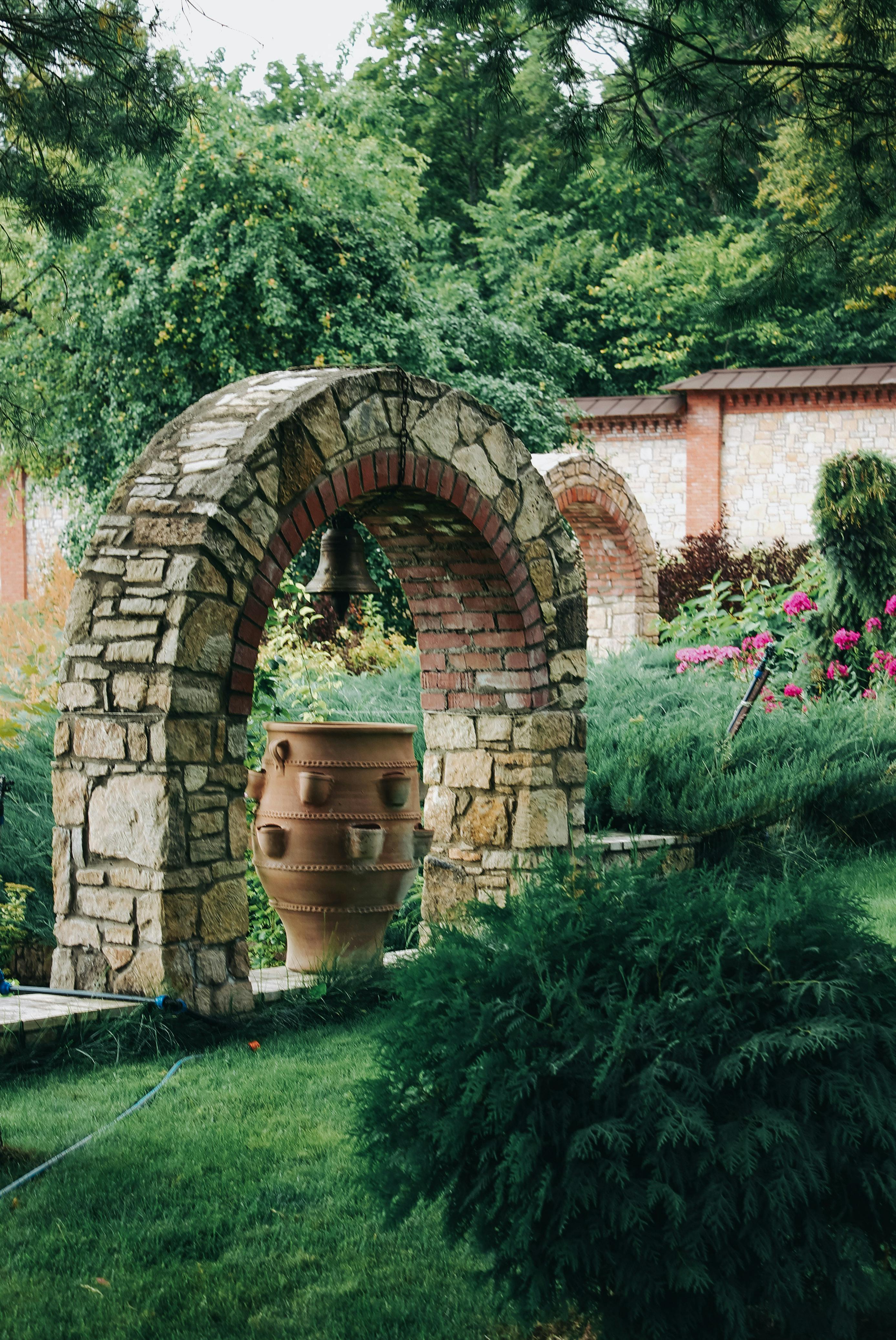 A stone archway surrounded by lush greenery and vibrant flowers in a tranquil garden scene.