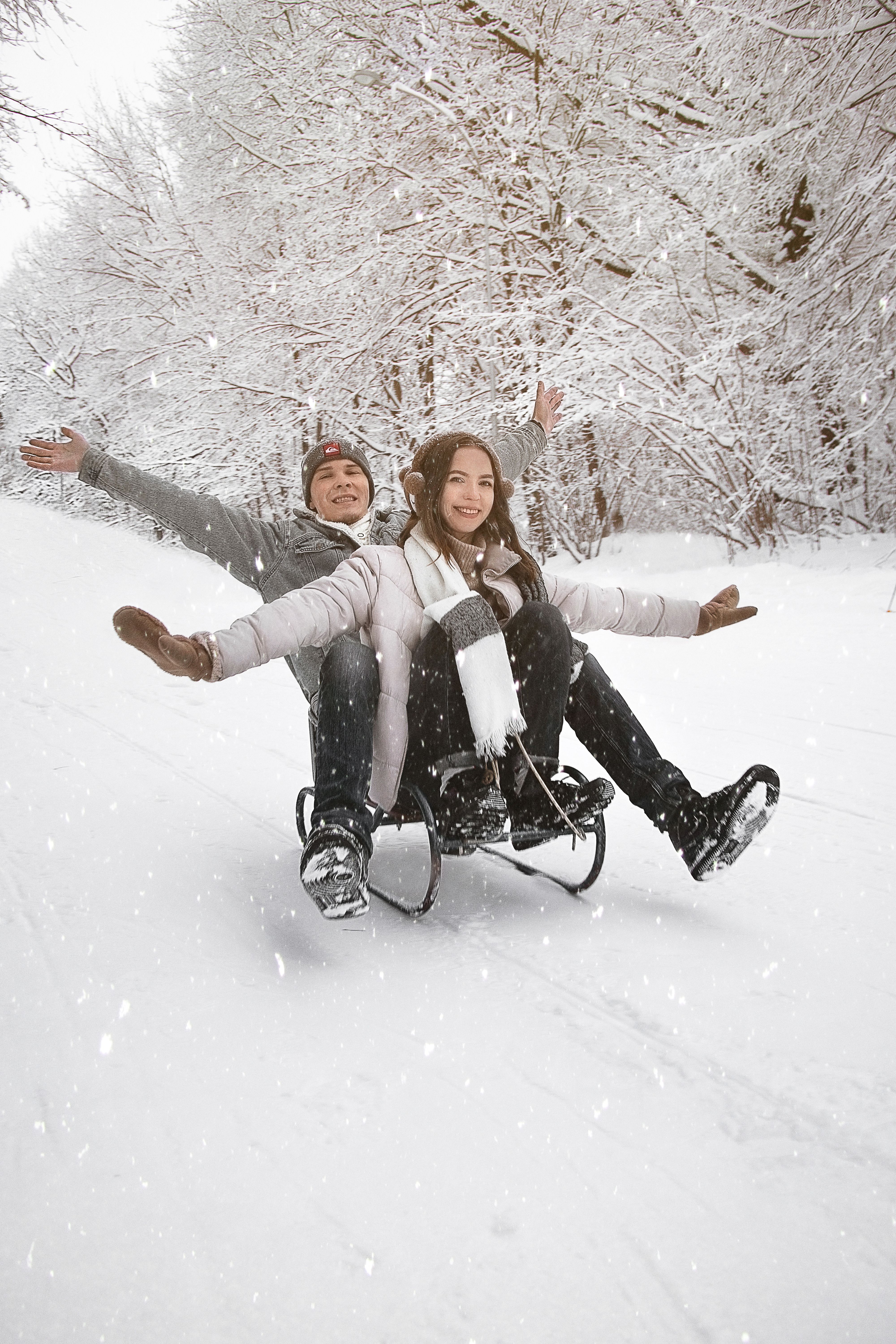 A cheerful couple sledding in a snowy forest, enjoying a fun winter activity together.