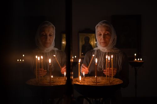 Free Elderly woman lighting candles in a dimly lit church, reflecting prayerfully. Stock Photo
