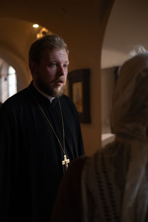 Free Orthodox priest attentively listens to a parishioner in a dimly lit church setting. Stock Photo
