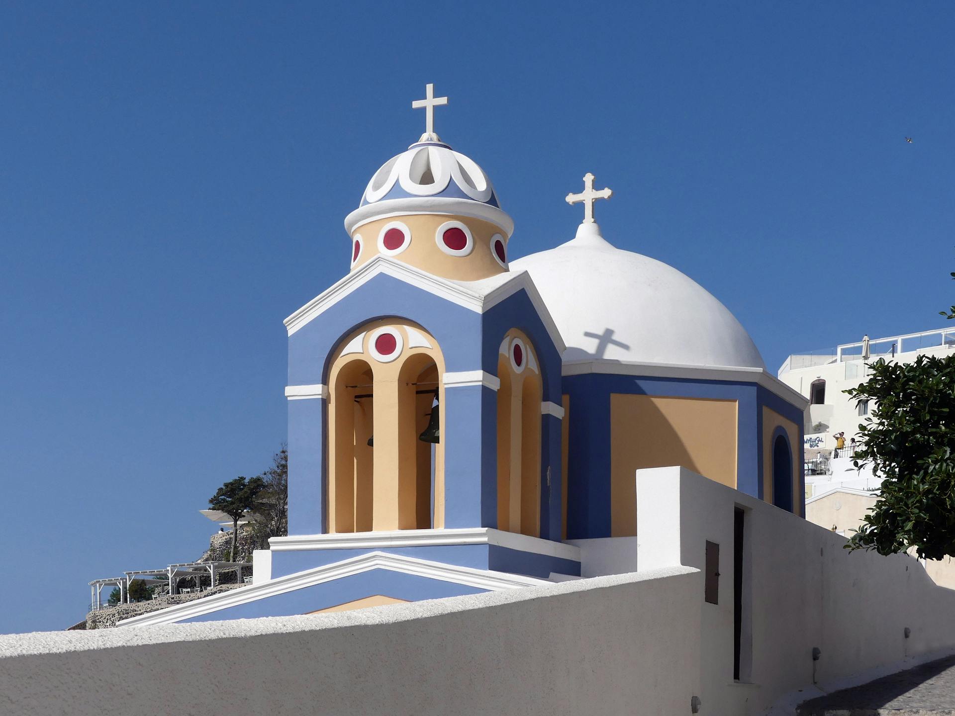Charming Greek Orthodox church with colorful architecture in Fira, Santorini, under a clear blue sky.