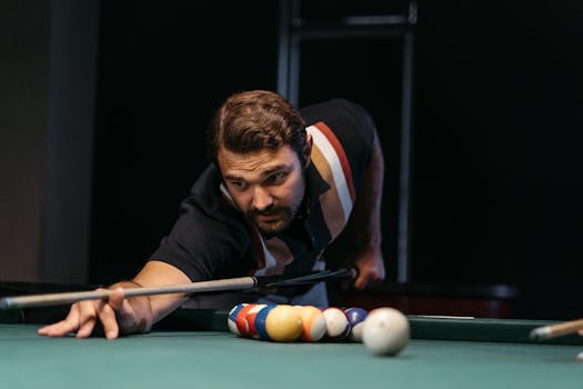 Focused man playing billiards, aiming a shot on a pool table indoors, epitomizing concentration and skill.