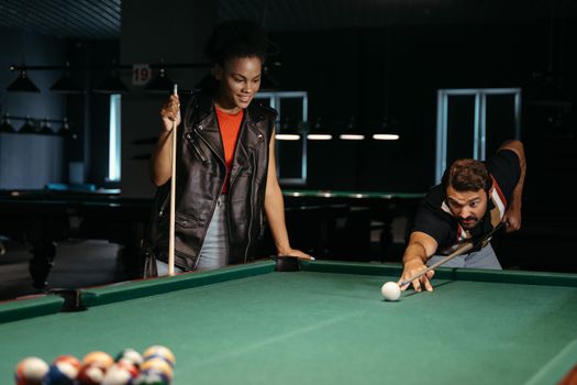 Two friends enjoy a game of billiards in a dimly lit pool hall, focused and having fun.
