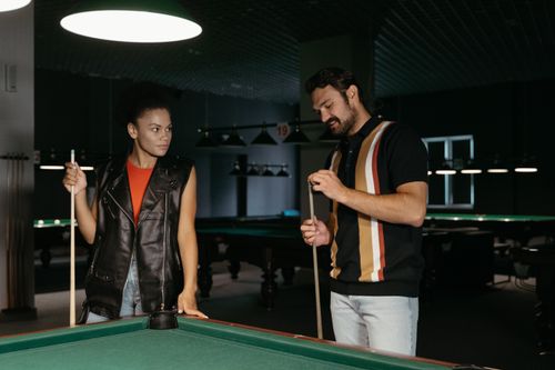 Free A man and woman holding cue sticks at a billiard table in a dimly lit pool hall. Stock Photo