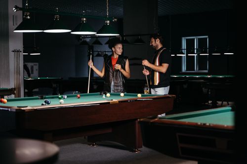 Free A male and female enjoying a friendly game of billiards in a dimly lit pool hall. Stock Photo