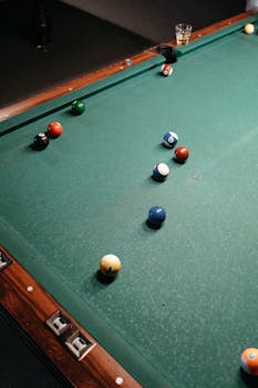 Billiard balls arranged on a green pool table in a dimly lit room.