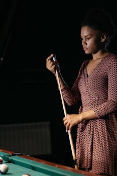 African American woman holding cue stick by billiard table indoors.