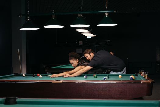 Man and woman focused on a billiard game in a cozy, dimly lit bar setting.