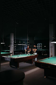 Two adults playing billiards on a dimly lit table, creating an intimate atmosphere.