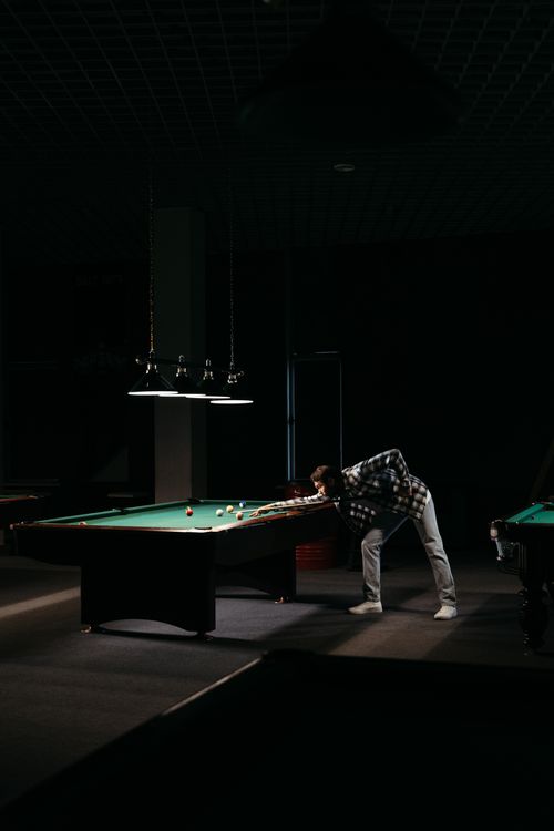 Free A man skillfully aiming at a billiard table under dim lighting indoors. Stock Photo