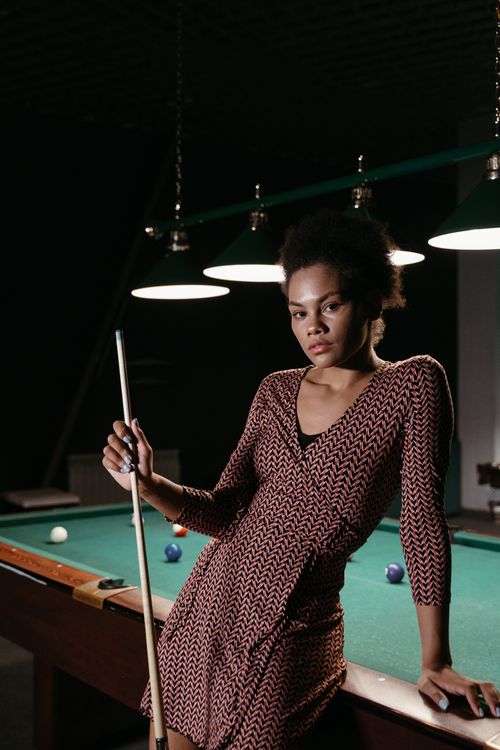 Free Portrait of a stylish woman holding a cue stick by a billiard table indoors. Stock Photo