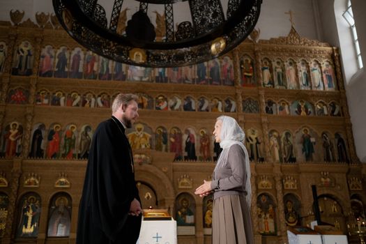 A priest and a parishioner engage in conversation inside an ornate Orthodox church.