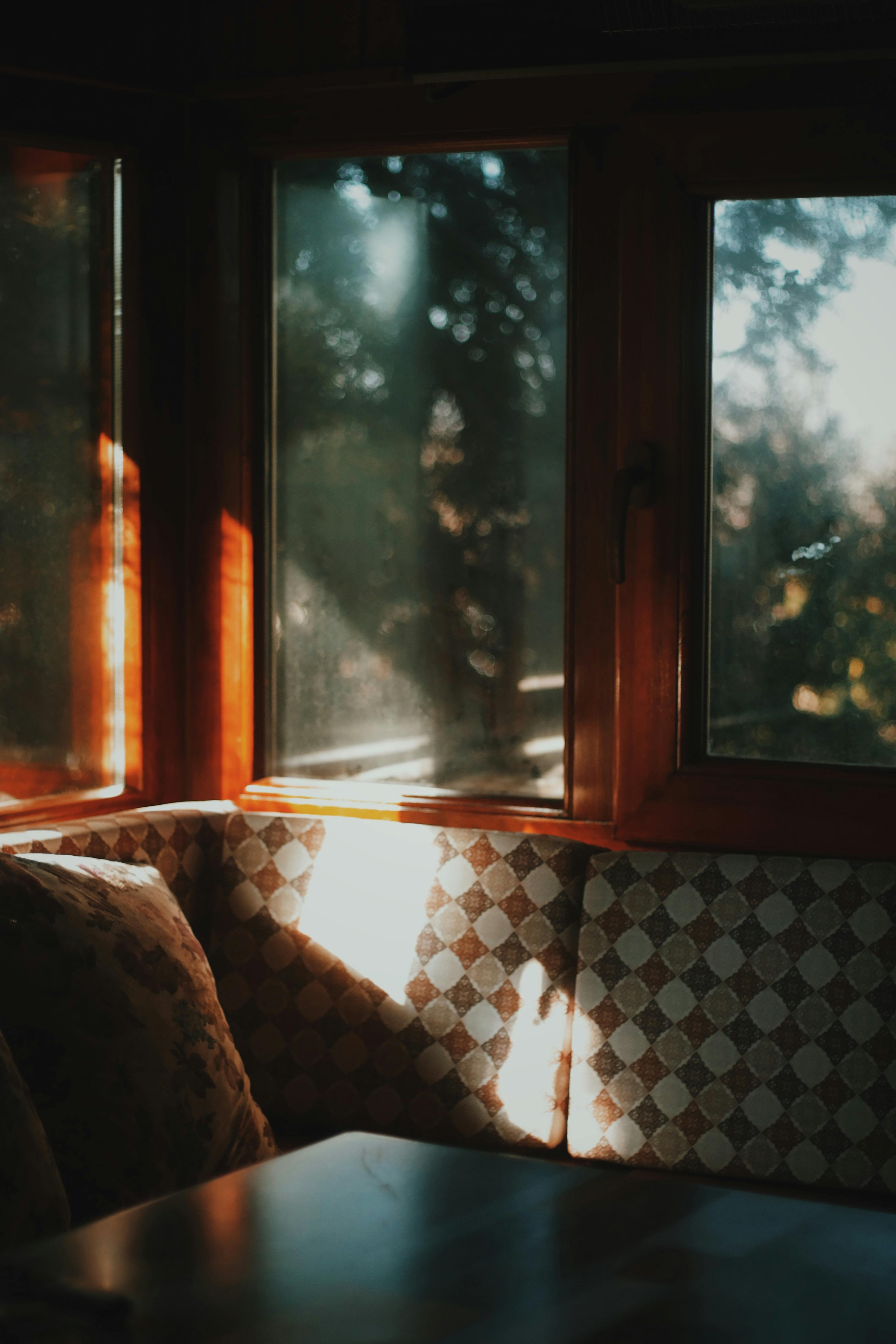 Free Warm sunlight streams through windows in a cozy corner with cushioned seating, accented by wooden frames. Stock Photo