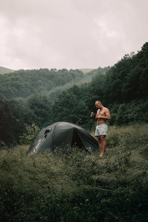 Man Standing Next to Tent in Green Mountains 