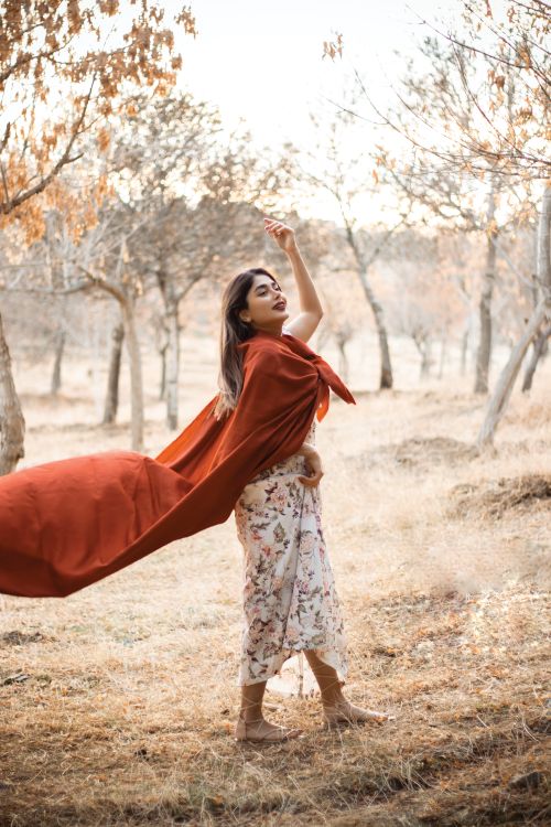 Free Woman standing in an autumn forest wearing a flowing red cape, surrounded by fall foliage. Stock Photo