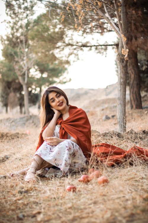 Free A young woman in a floral dress sits serenely in a scenic forest, wrapped in a red shawl, during autumn. Stock Photo