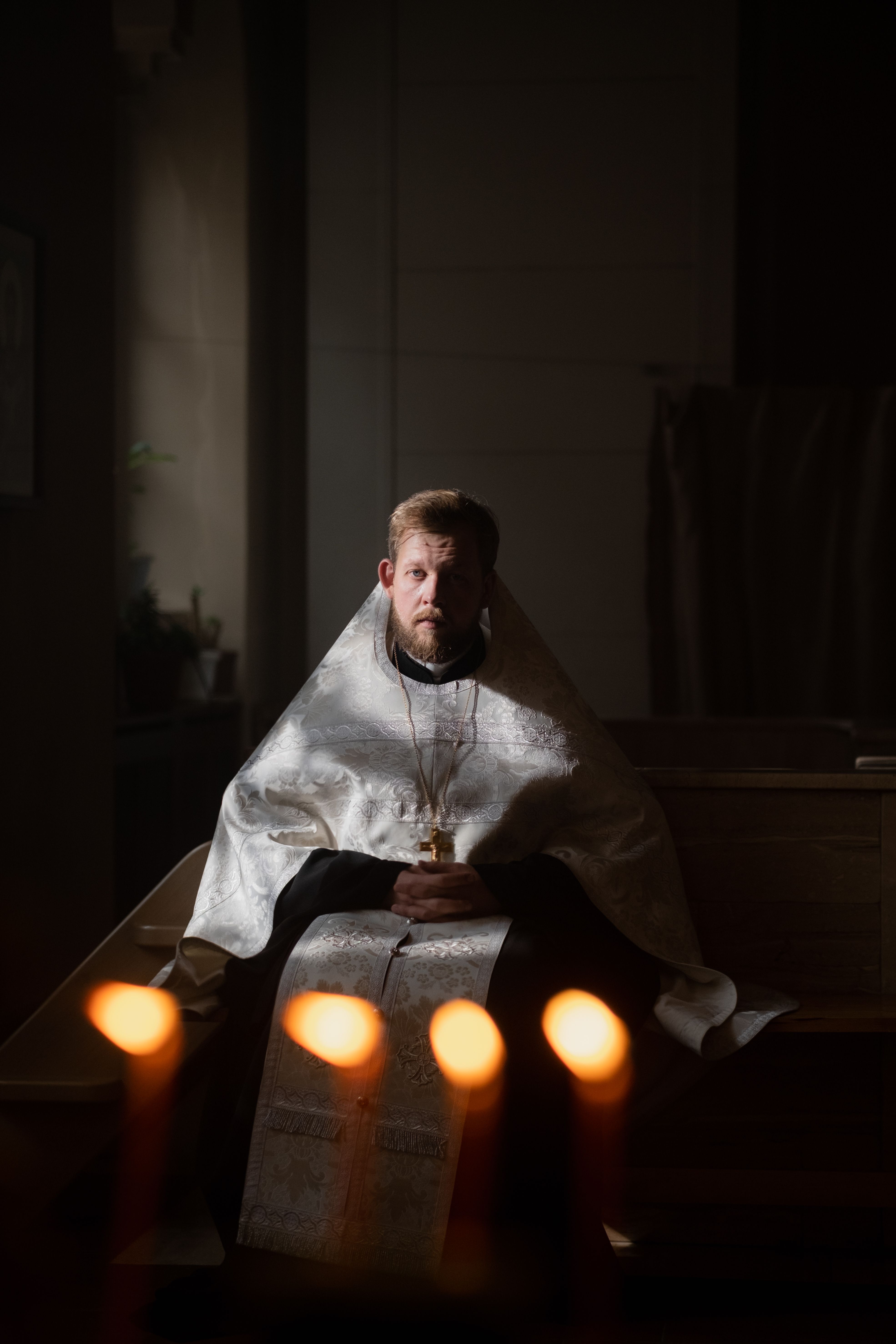 A contemplative Orthodox priest sitting in a dimly lit church, surrounded by candlelight.