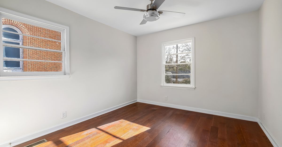 Well-lit empty room featuring wooden flooring and a ceiling fan, ideal for apartments or home staging.