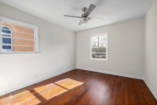 Well-lit empty room featuring wooden flooring and a ceiling fan, ideal for apartments or home staging.