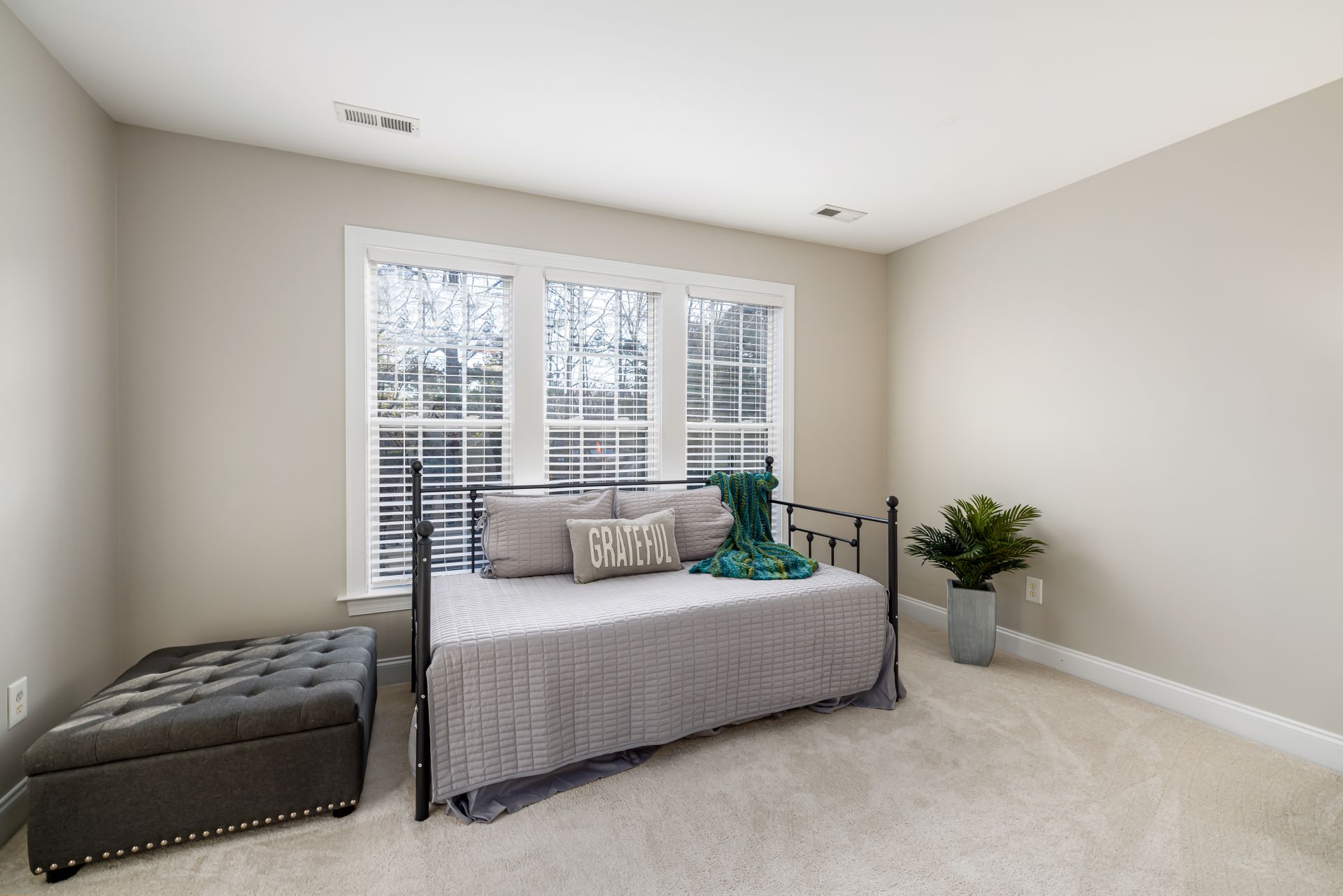 Spacious bedroom with daybed and minimalist decor, featuring a 'Grateful' pillow and bright natural light.