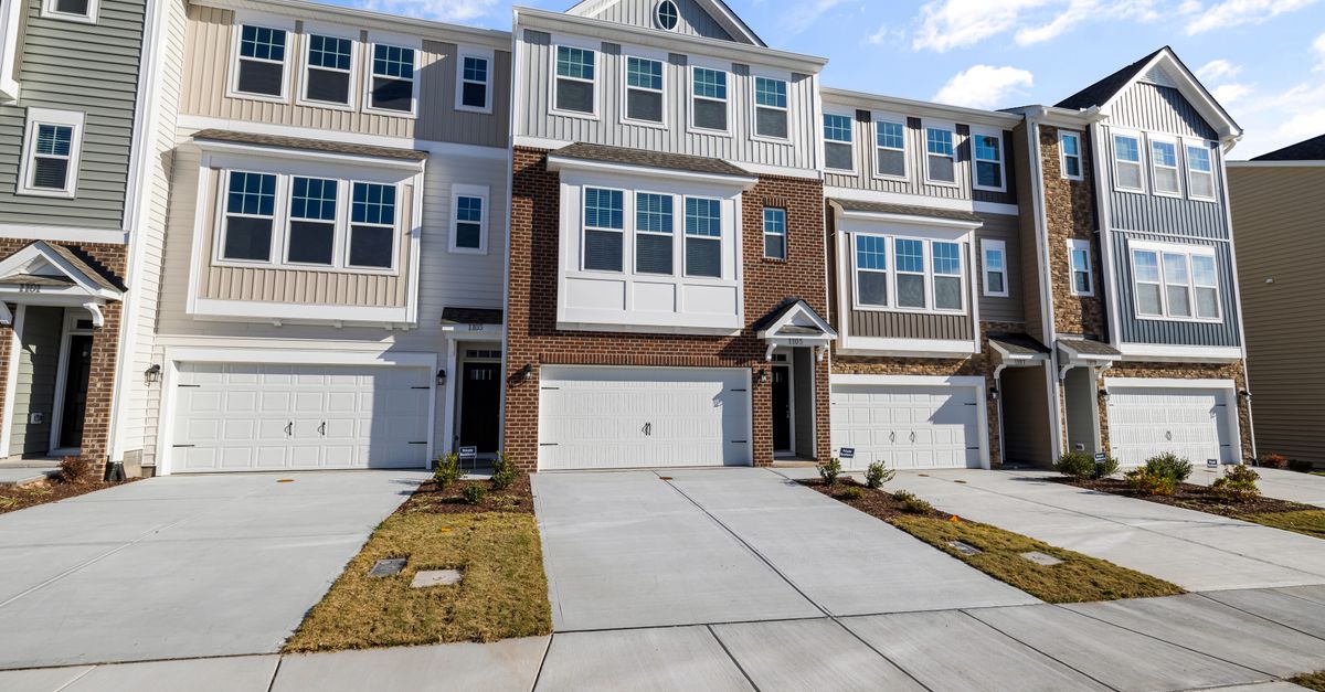 A row of modern suburban townhouses with clean driveways and blue sky backdrop.