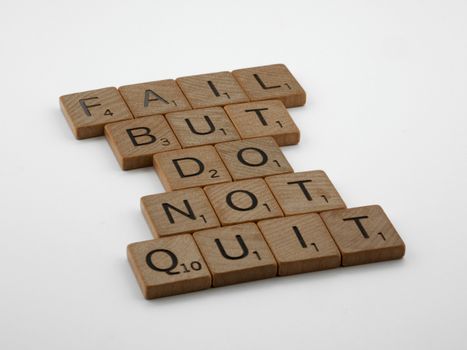 Close-up of Scrabble tiles forming the motivational phrase 'Fail but do not quit' on a white surface.