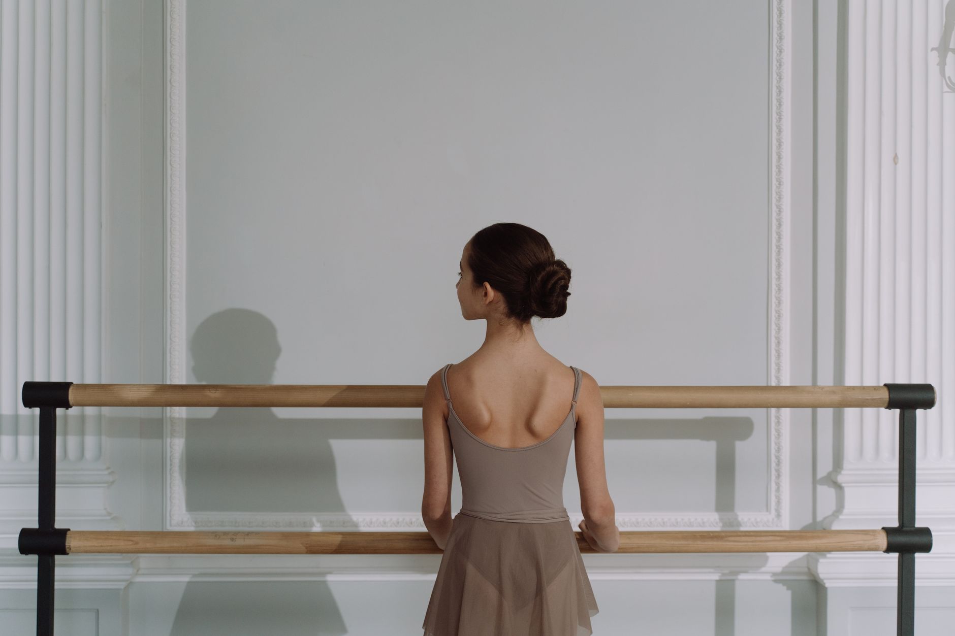 Back view of a young ballerina standing at ballet barre in a class.