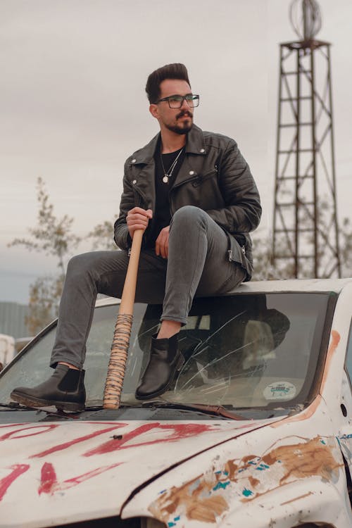Man in Black Leather Jacket holding a Baseball Bat sitting in an Abandoned Car 