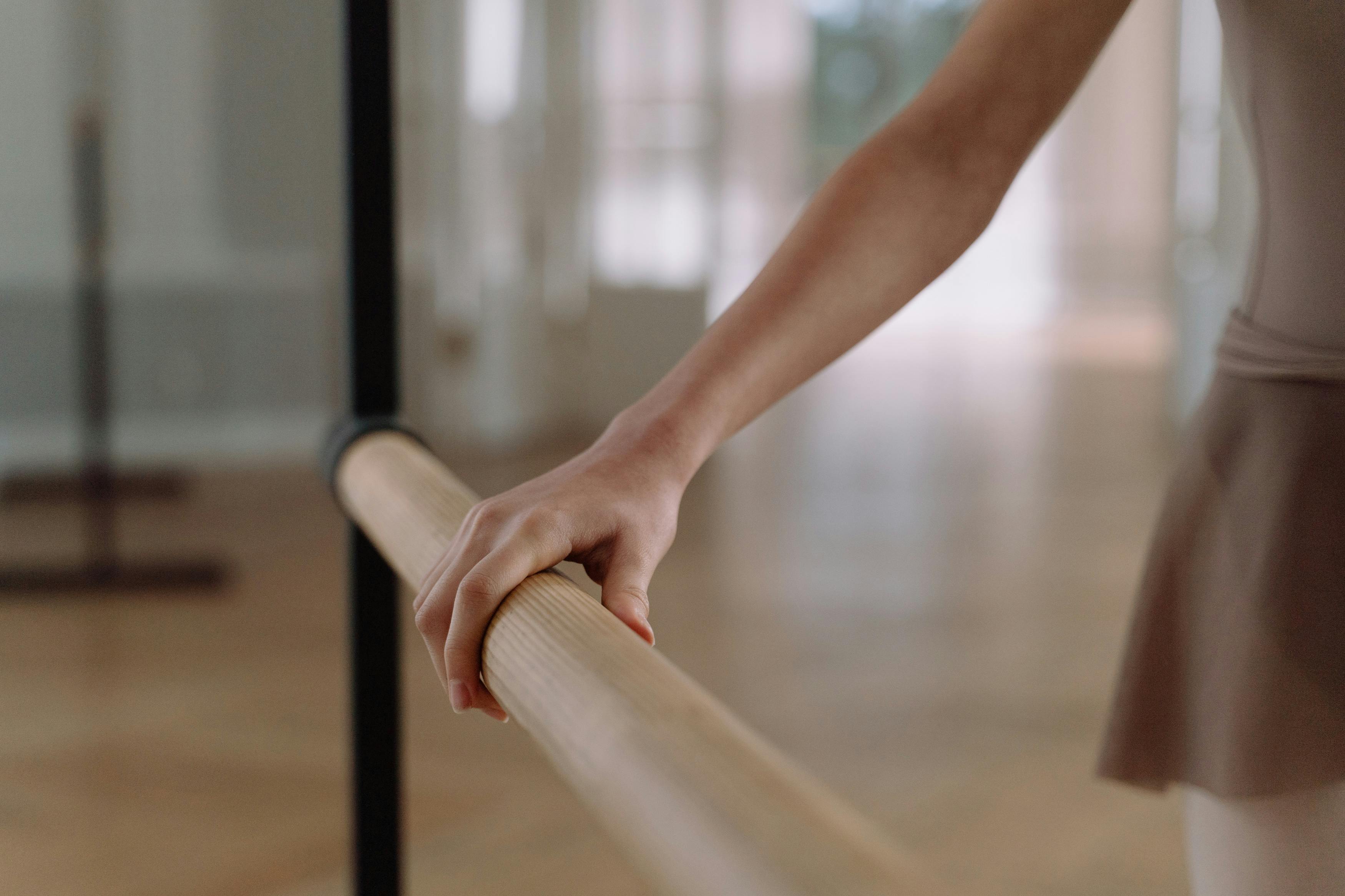 Close-up of a ballet dancer's hand holding a wooden barre in a dance studio.