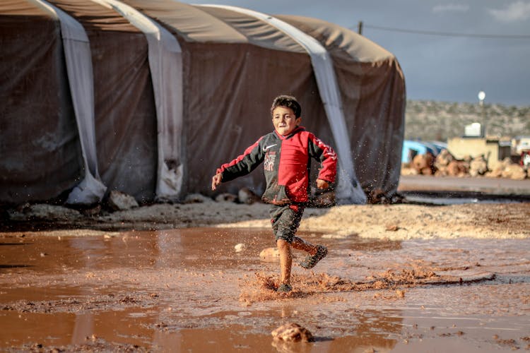 Young Boy Running In A Muddy Puddle