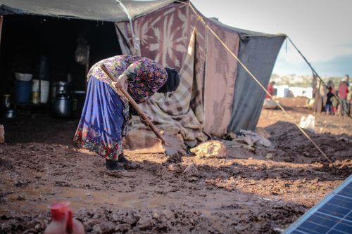 Free Elderly woman shoveling mud outside a tent in an Idlib refugee camp, Syria. Stock Photo