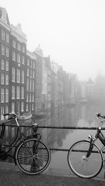 Black and white photo of bicycles parked on a canal bridge in foggy Amsterdam.