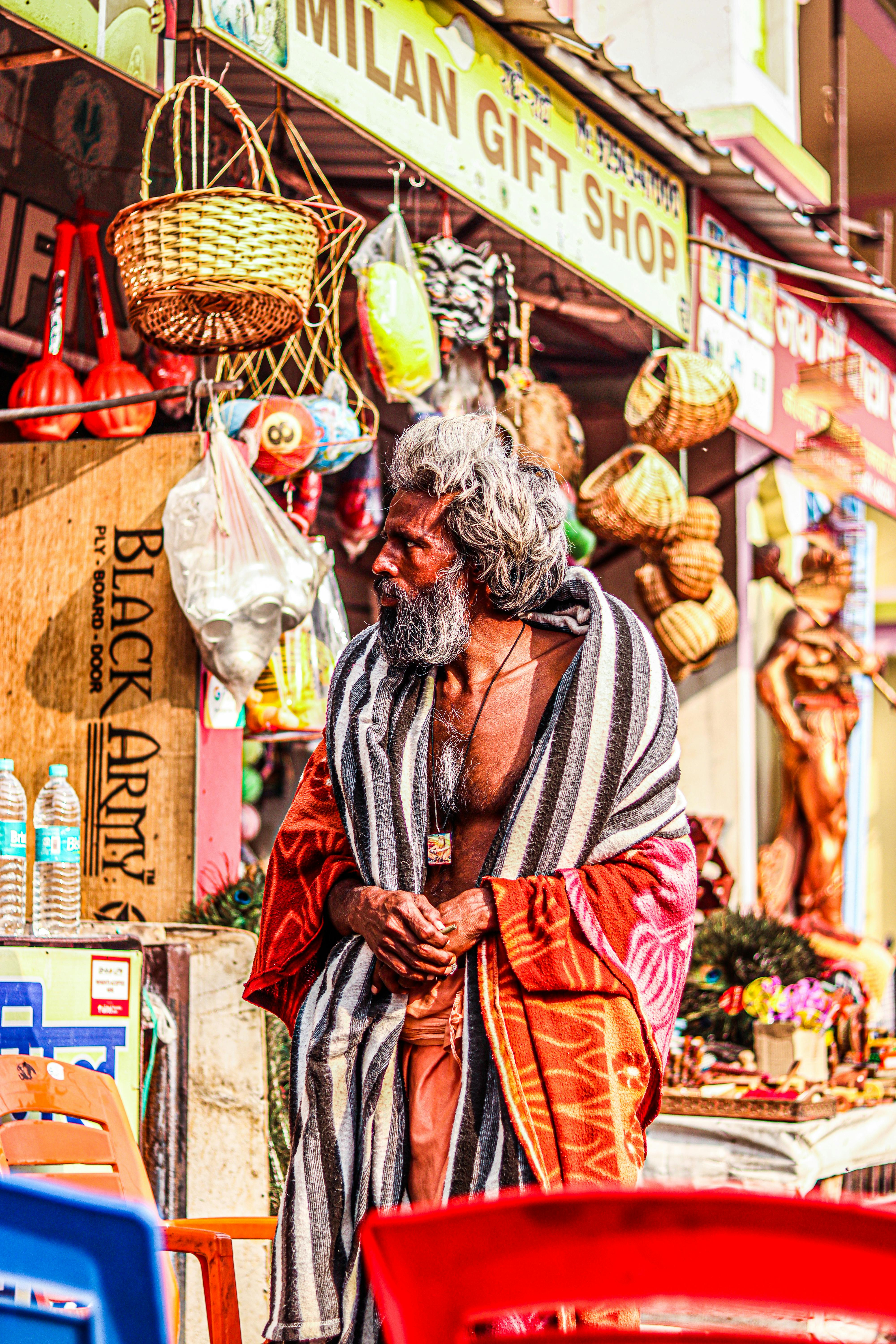 Elderly man in a colorful market surrounded by vibrant objects and local crafts.