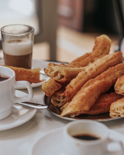 Free Close-up of crispy churros with coffee on a table setting in Spain, ideal for food and travel themes. Stock Photo