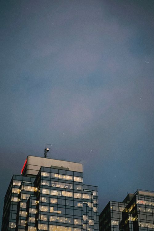 Free Low-angle view of glass skyscrapers with lit windows under a cloudy evening sky, ideal for modern cityscapes. Stock Photo