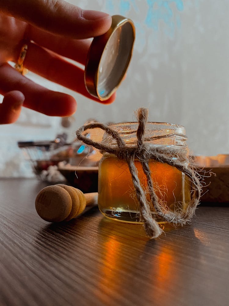 A Close-Up Shot Of A Person Opening A Jar Of Honey