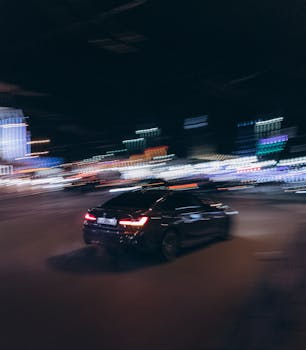 Blurred motion of a black car driving through a vibrant city street at night.