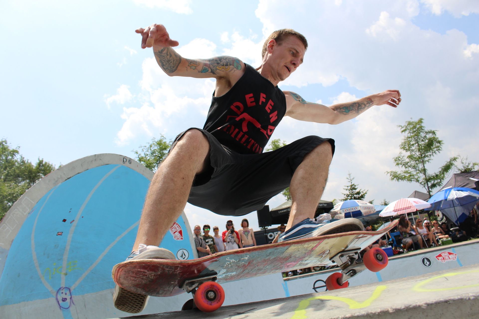 Skateboarder performing an action-packed stunt at an outdoor skatepark on a sunny day.