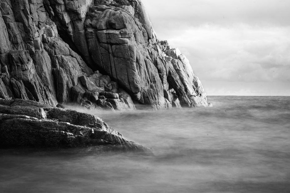 Moody black and white photo of coastal cliffs with crashing waves.