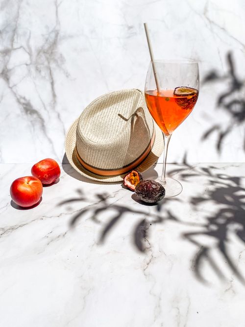 Free A refreshing Aperol spritz with peaches and a straw hat on marble in summer sunlight. Stock Photo