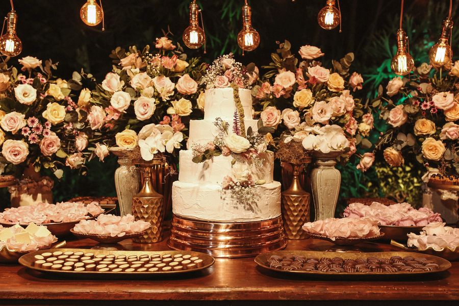 Multi-tiered white wedding cake surrounded by flower vases and candles