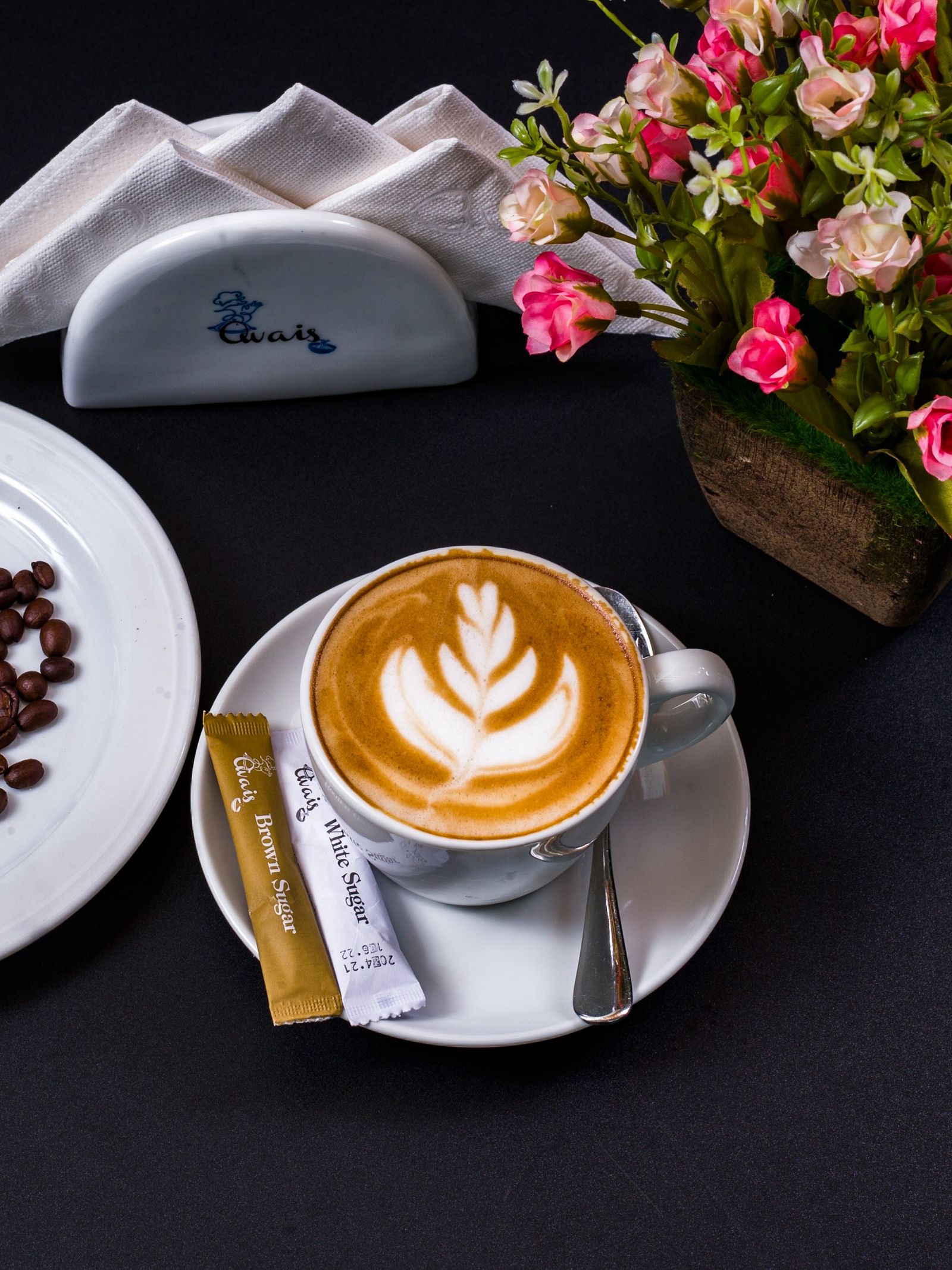 A cup of latte art surrounded by coffee beans and fresh flowers