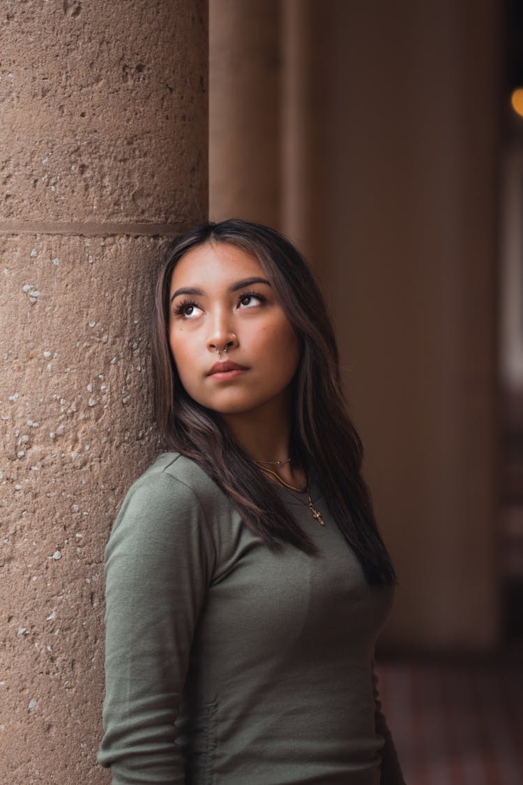 Young Woman In Gray Long Sleeve Shirt Leaning On Brown Column