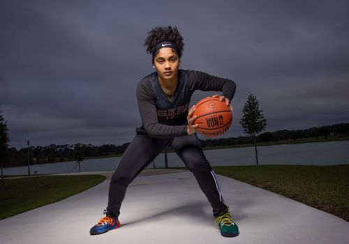 An athletic woman poses with a basketball, showcasing readiness and skill on an outdoor court.